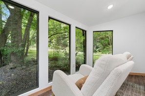 Une chambre moderne avec de grandes fenêtres, une chaise blanche et une vue sur une forêt.