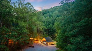 Un chalet entouré d’une forêt dense, avec un chemin de gravier menant à l’entrée.