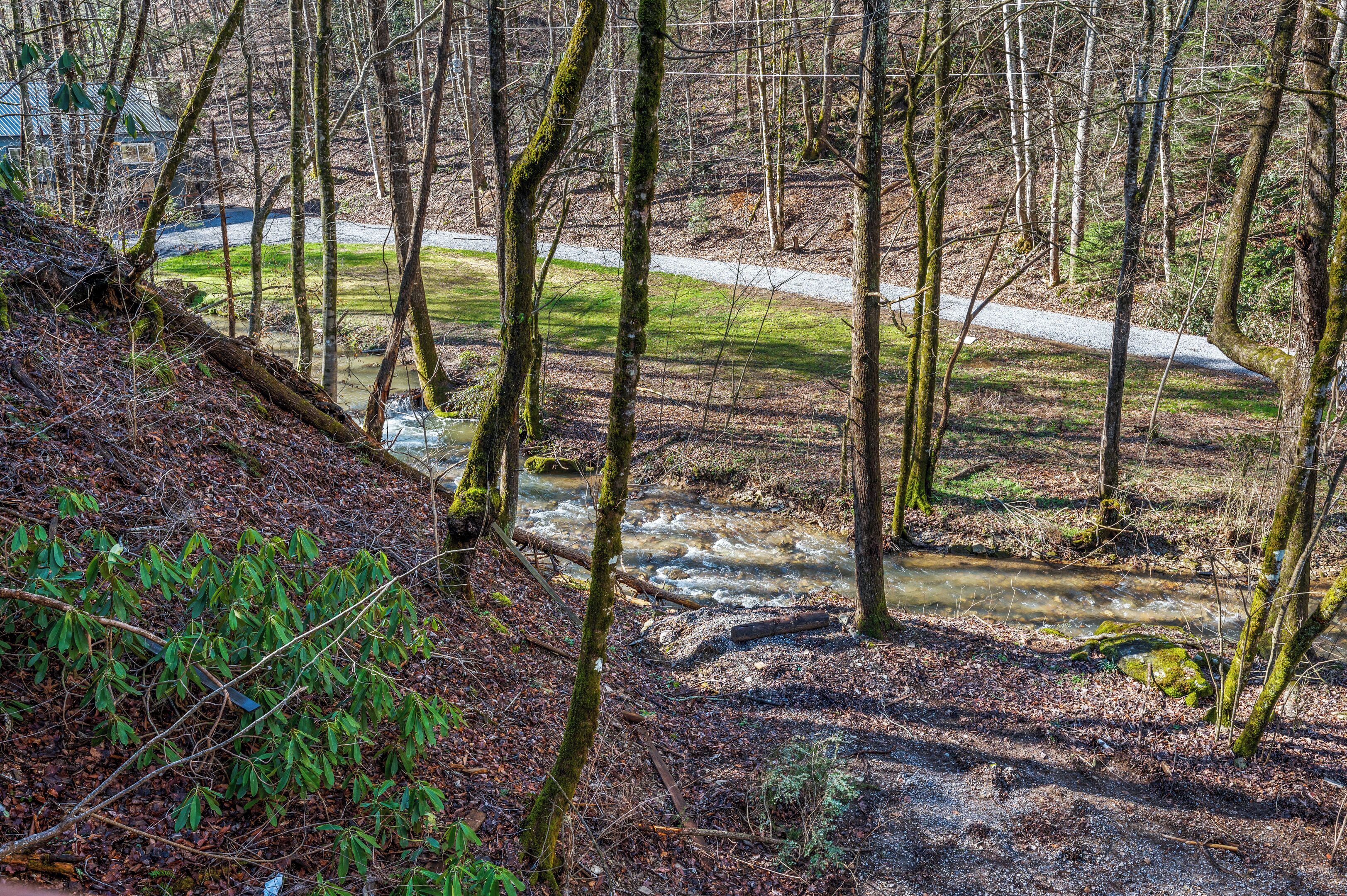 Une zone boisée avec un ruisseau, un sentier de gravier et un bâtiment en arrière-plan.