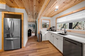 A modern kitchen with stainless steel appliances, wooden ceiling, and a large window. - Creekside Lodge on 6 Acres | Game Room, 8-Person Hot Tub, Sleeps 17 (Sevierville)