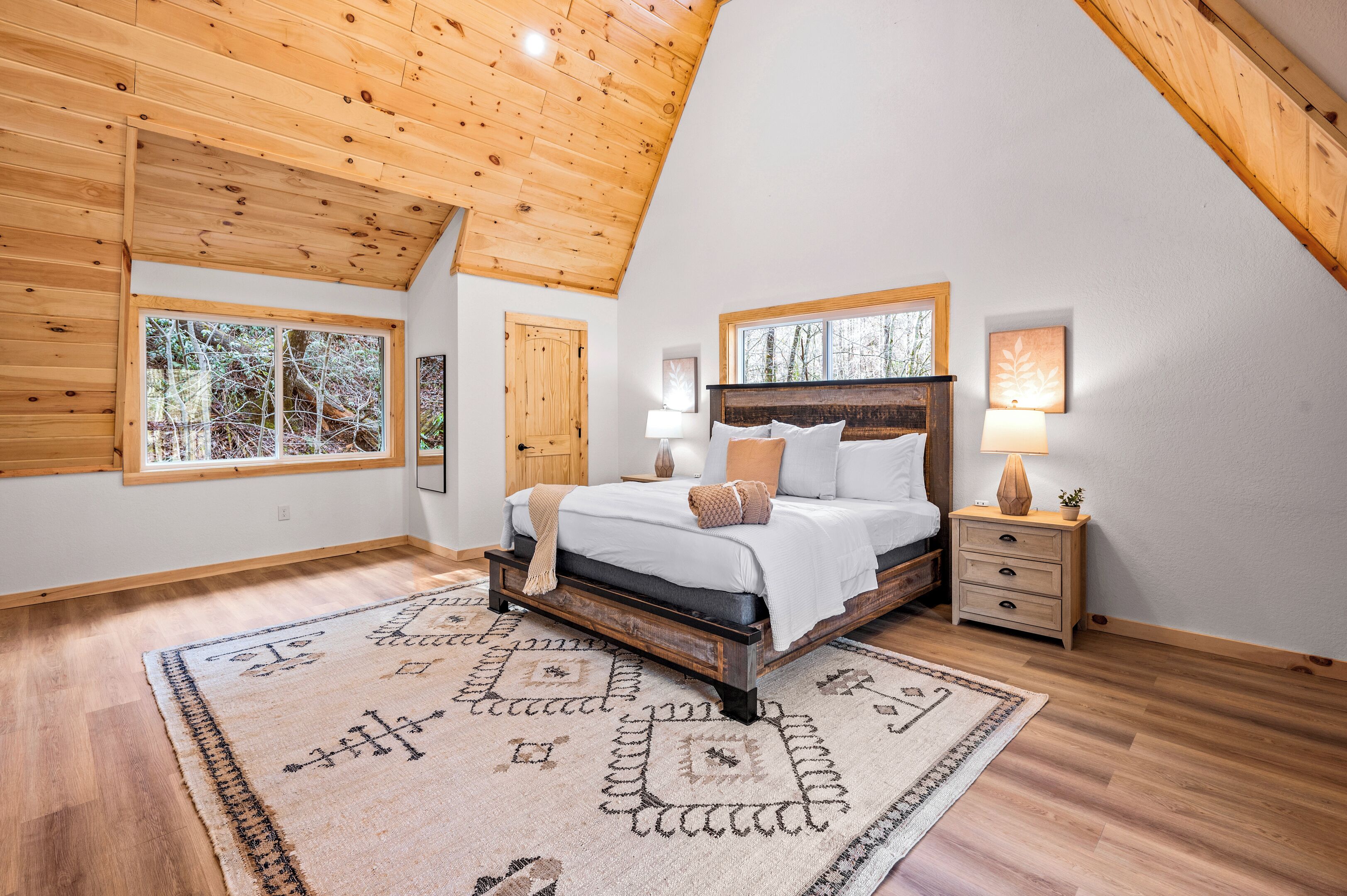 Une chambre avec un plafond en pente, un plancher en bois, un lit avec une tête de lit, une table de chevet et un tapis.