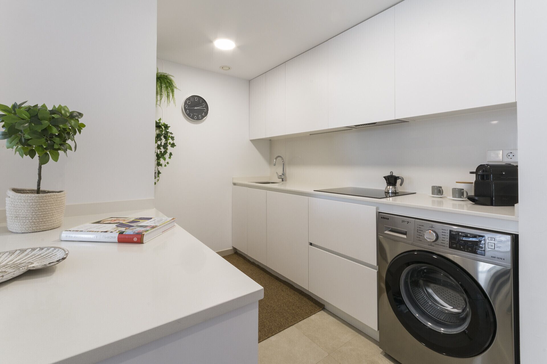 Una cocina moderna con lavadora integrada, un lavabo y un reloj en la pared.