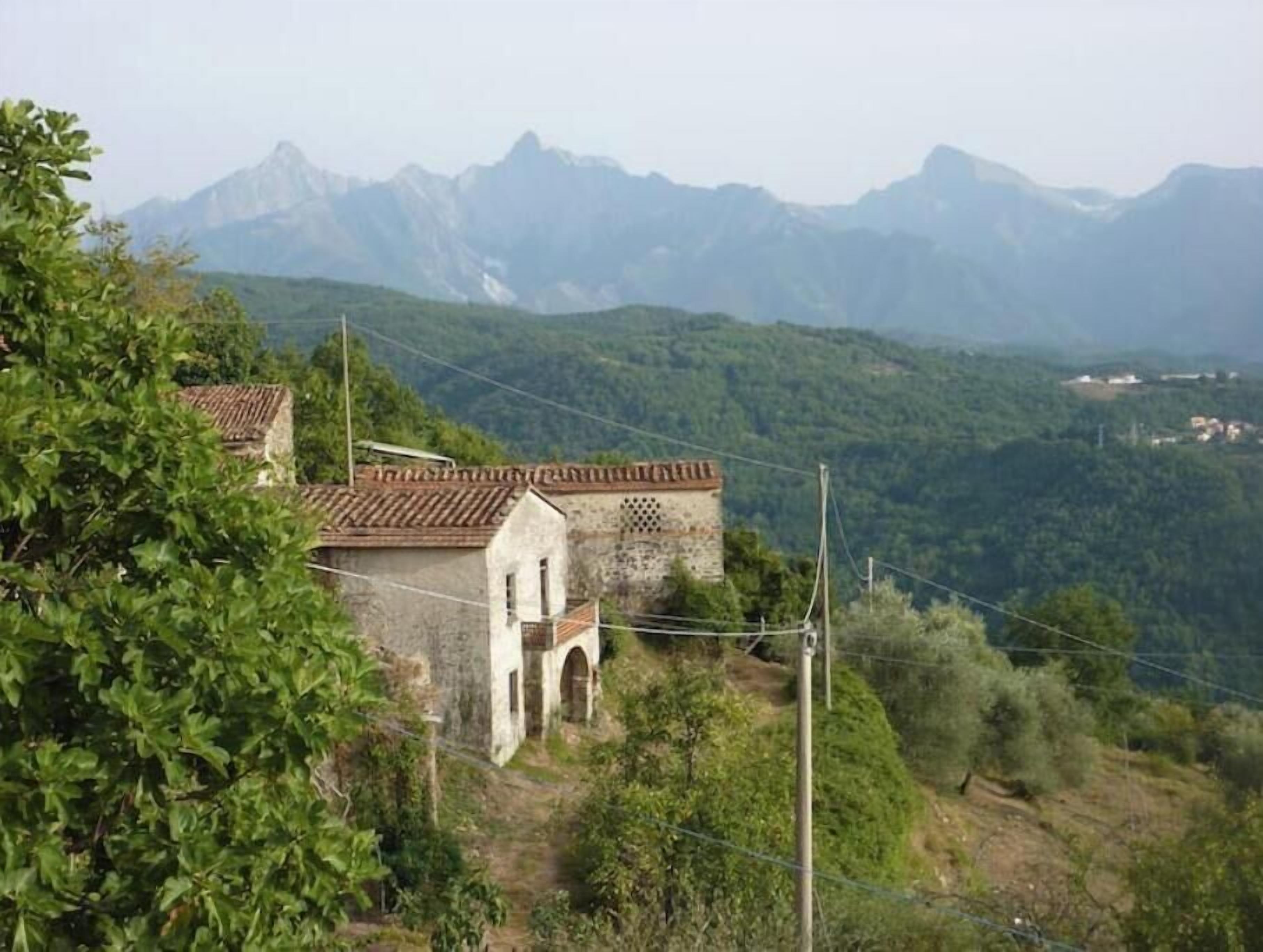 Ein rustikales Steinhaus mit Ziegeldach, umgeben von üppiger Vegetation und Bergen im Hintergrund.