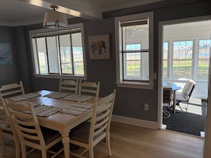 Comedor con una mesa lista para cuatro, dos ventanas y una puerta que da al exterior.