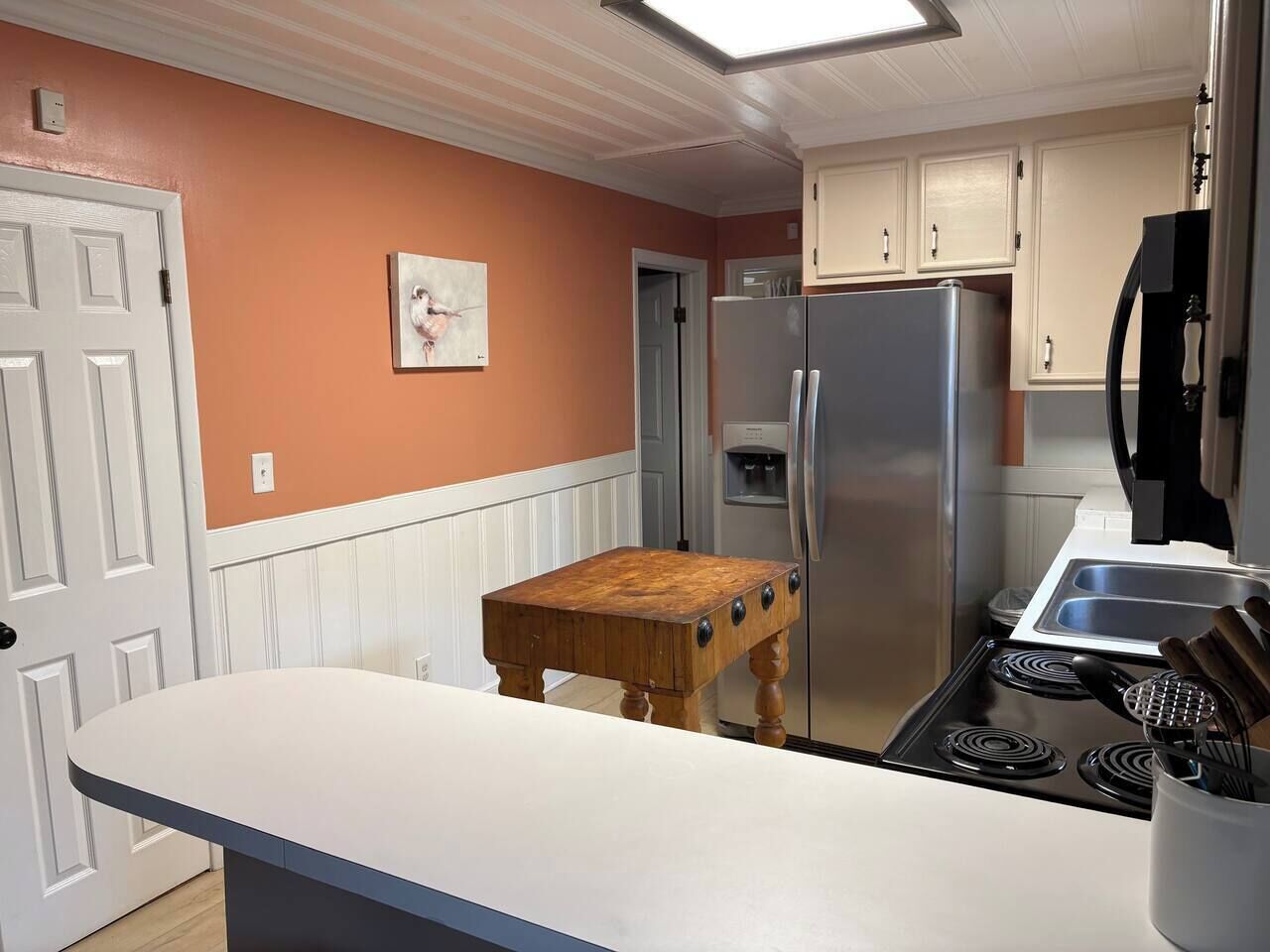 A kitchen with a white countertop, a wooden table, a refrigerator, and a stove.