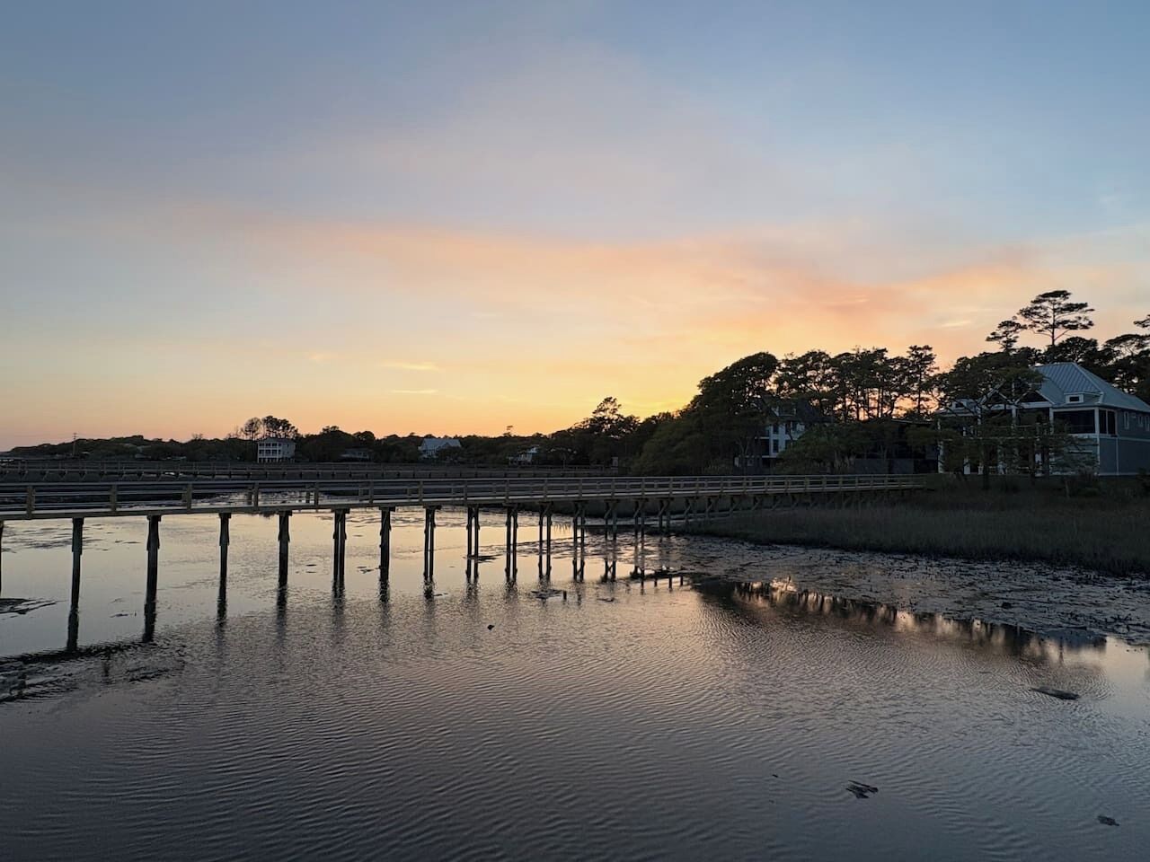 A waterfront scene with a bridge, calm water, and a building in the background.