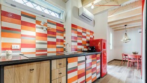 Una cocina moderna con un salpicadero a cuadros, armarios de madera, un refrigerador rojo y un comedor con sillas rosadas.