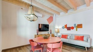 Una sala de estar moderna con una mesa redonda, sillas rosas, un sofá gris y un televisor.