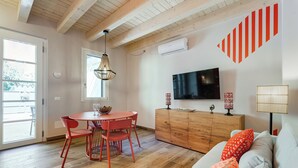 Una habitación con techo de madera, una mesa de comedor con sillas, un sofá, un televisor y un armario.