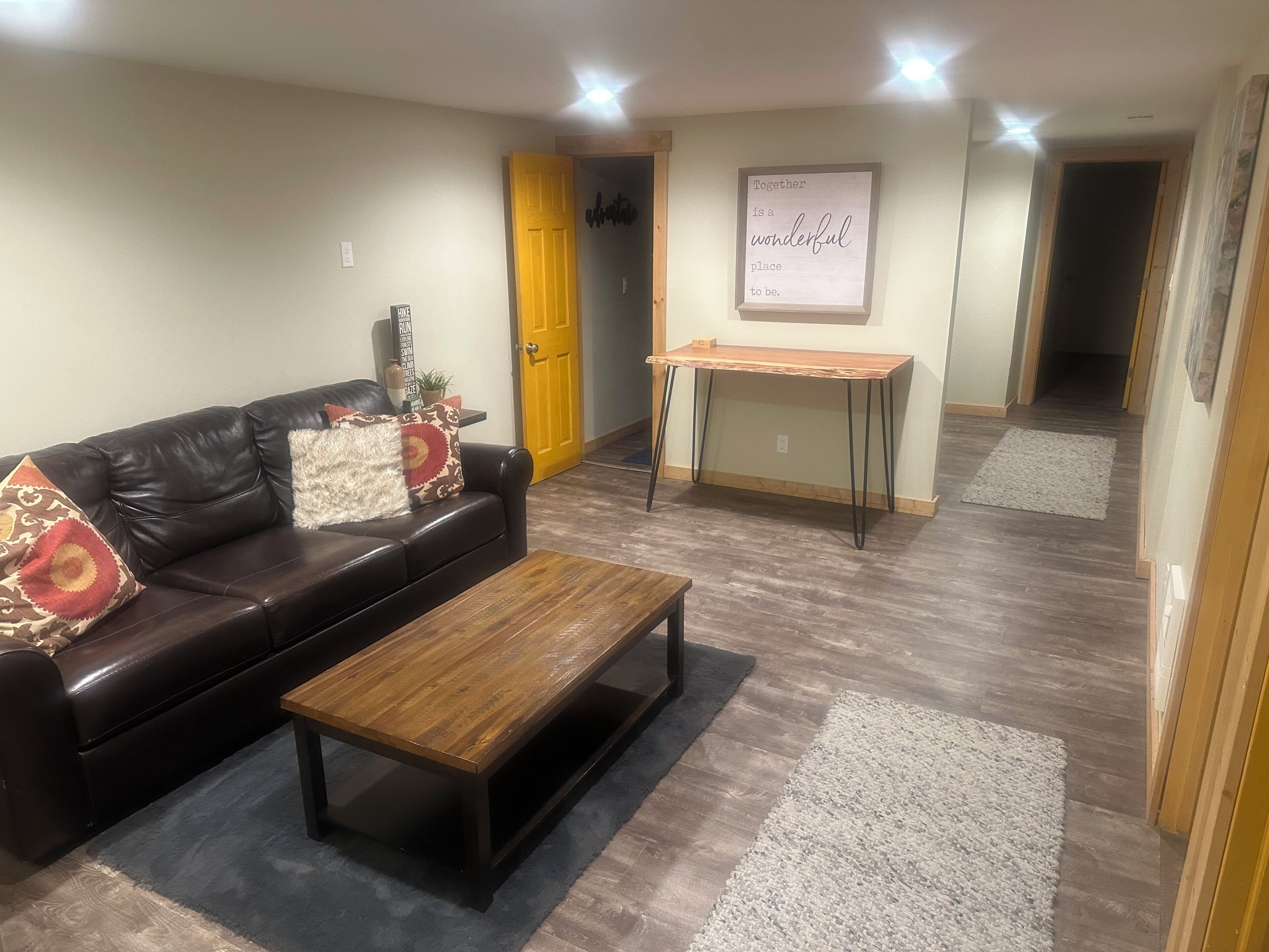 A living room with a dark leather sofa, a wooden coffee table, a small wooden side table, and a wall-mounted sign.