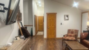 A spacious living room with a wooden floor, a television mounted on the wall, a sofa, a chair, and a wooden cabinet. - Spacious 6-bedroom house in McCall - walkable to Payette Lake, Shore Lodge (McCall)