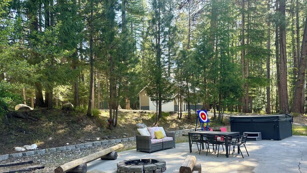 A patio with a fire pit, seating, and a hot tub in a forested area. - Spacious 6-bedroom house in McCall - walkable to Payette Lake, Shore Lodge (McCall)