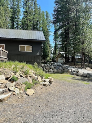 Une cabane avec une allée en gravier, entourée d’arbres et d’un mur de pierres.