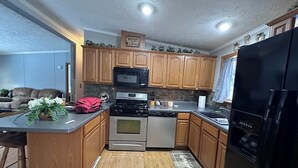 Cocina compacta con armarios de madera, estufa de acero inoxidable, microondas y refrigerador negro.