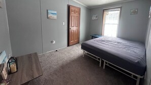 Un dormitorio con cama, puerta de madera, ventana y una mesita.