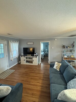 A living room with a flat-screen TV, a sofa, a coffee table, and a bookshelf. - Oceanside - Quick 5 min walk to the beach - Great porch (Salvo)