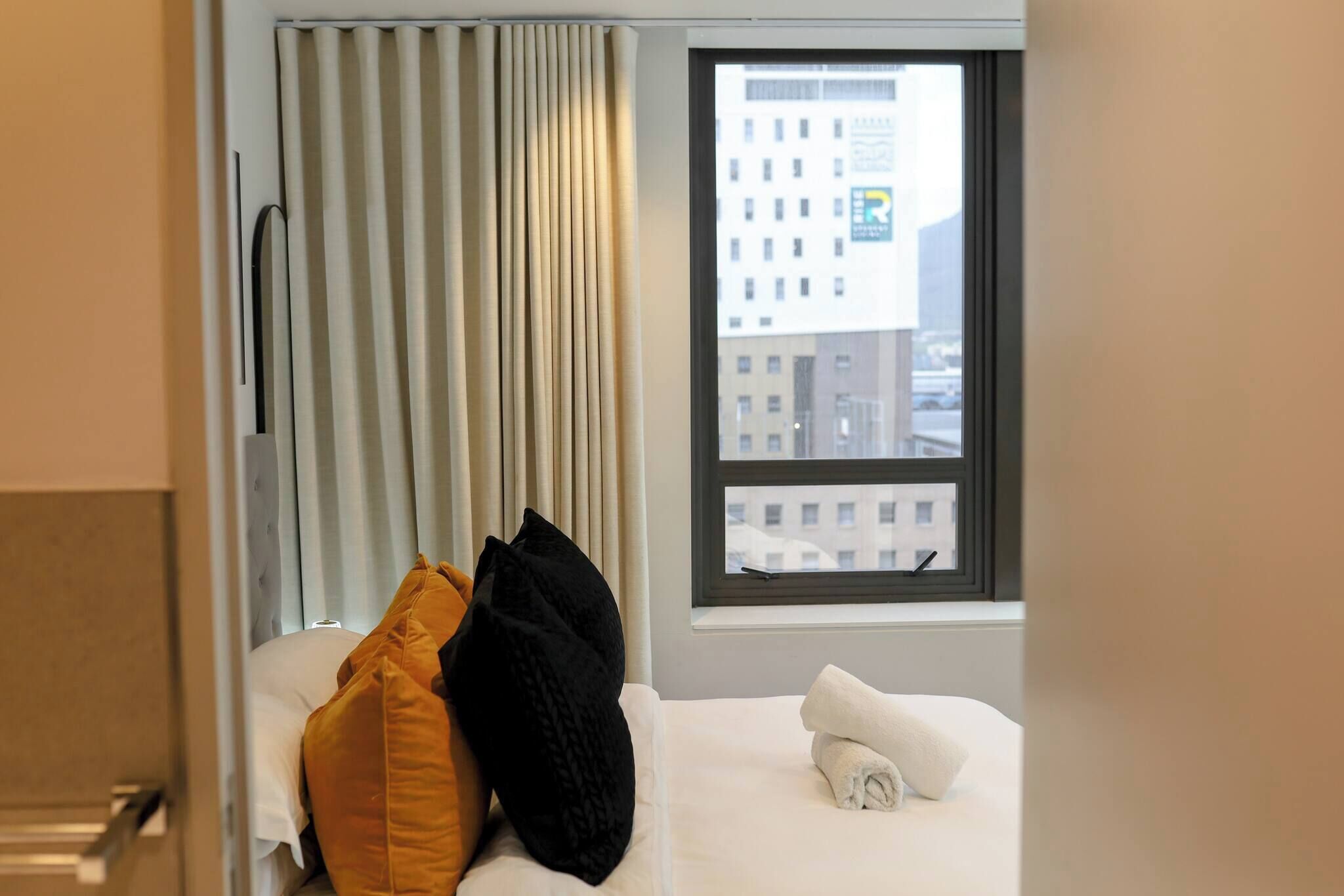 A hotel room with a bed, a window with a view of buildings, and a curtain.
