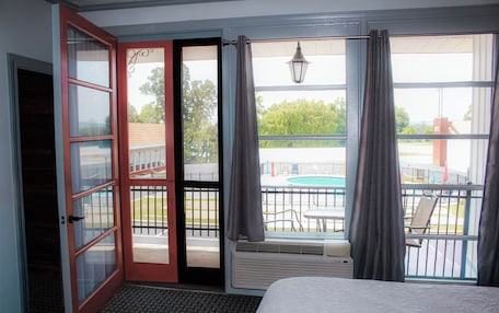 A hotel room with a bed, a sliding glass door leading to a balcony with a pool and outdoor furniture.
