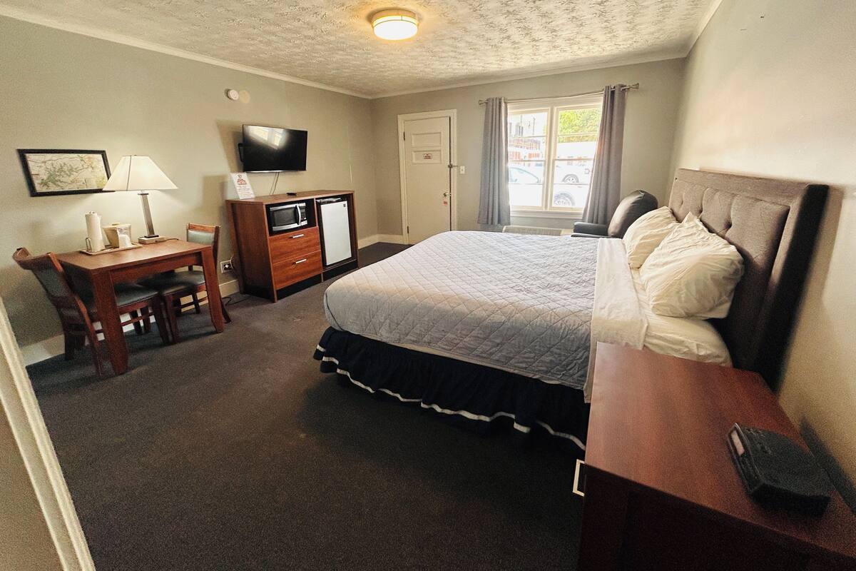 Une chambre d’hôtel comprenant un lit, un bureau avec une lampe, une télévision et une petite kitchenette.