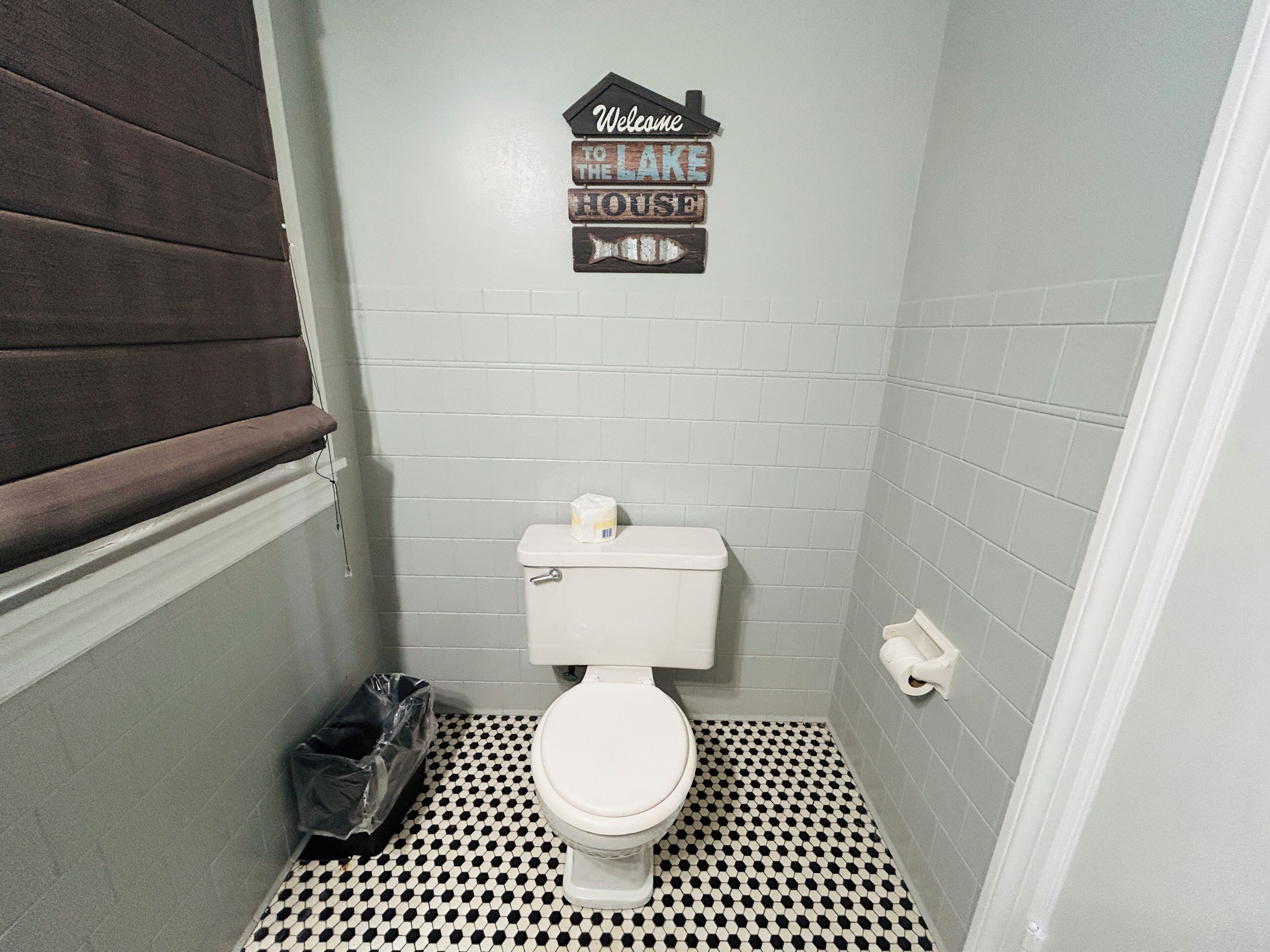 A small bathroom with a white toilet, a black and white checkered floor, and a welcome sign above the toilet.