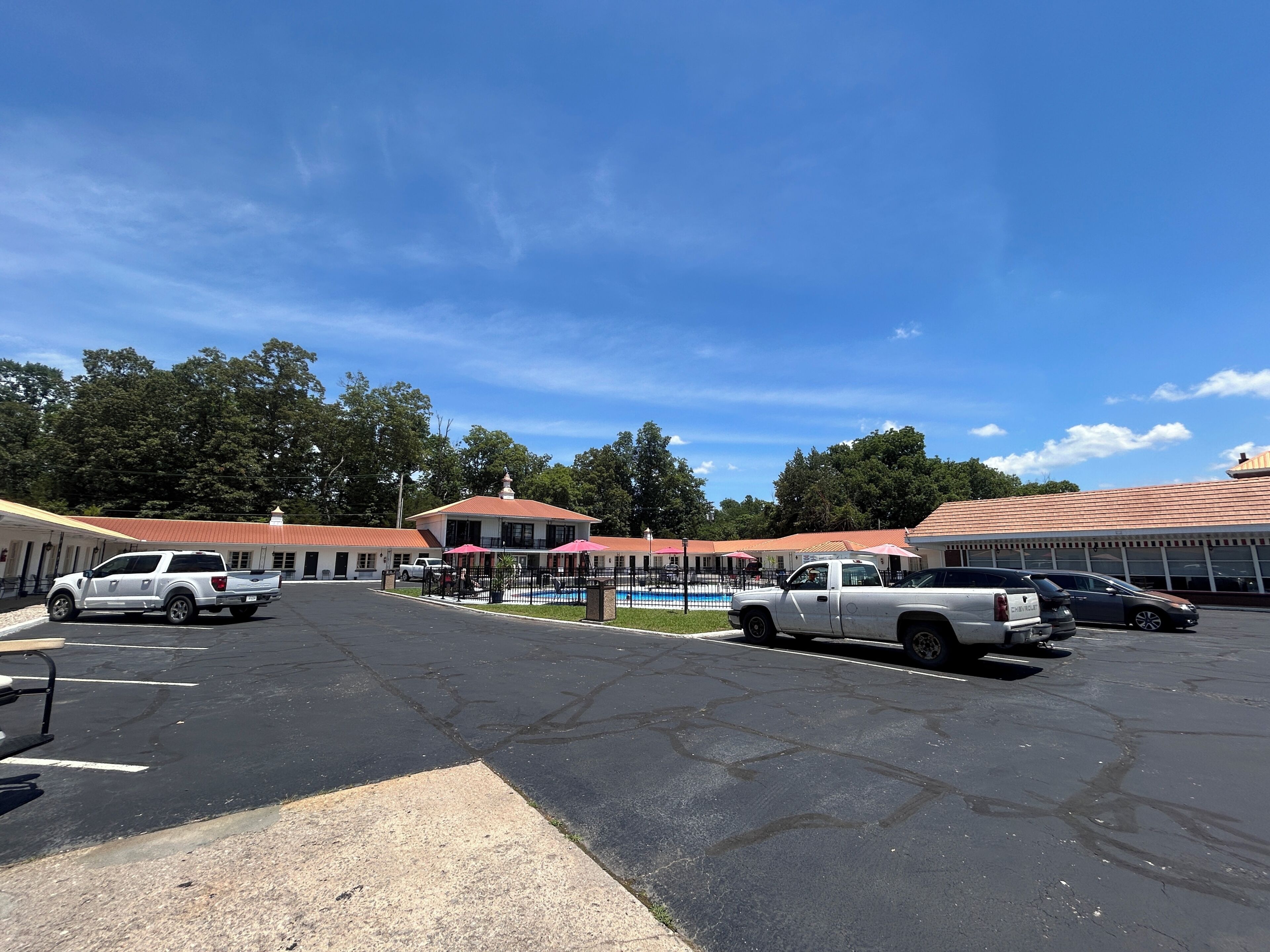 A parking lot with several vehicles, a swimming pool, and buildings with red roofs.