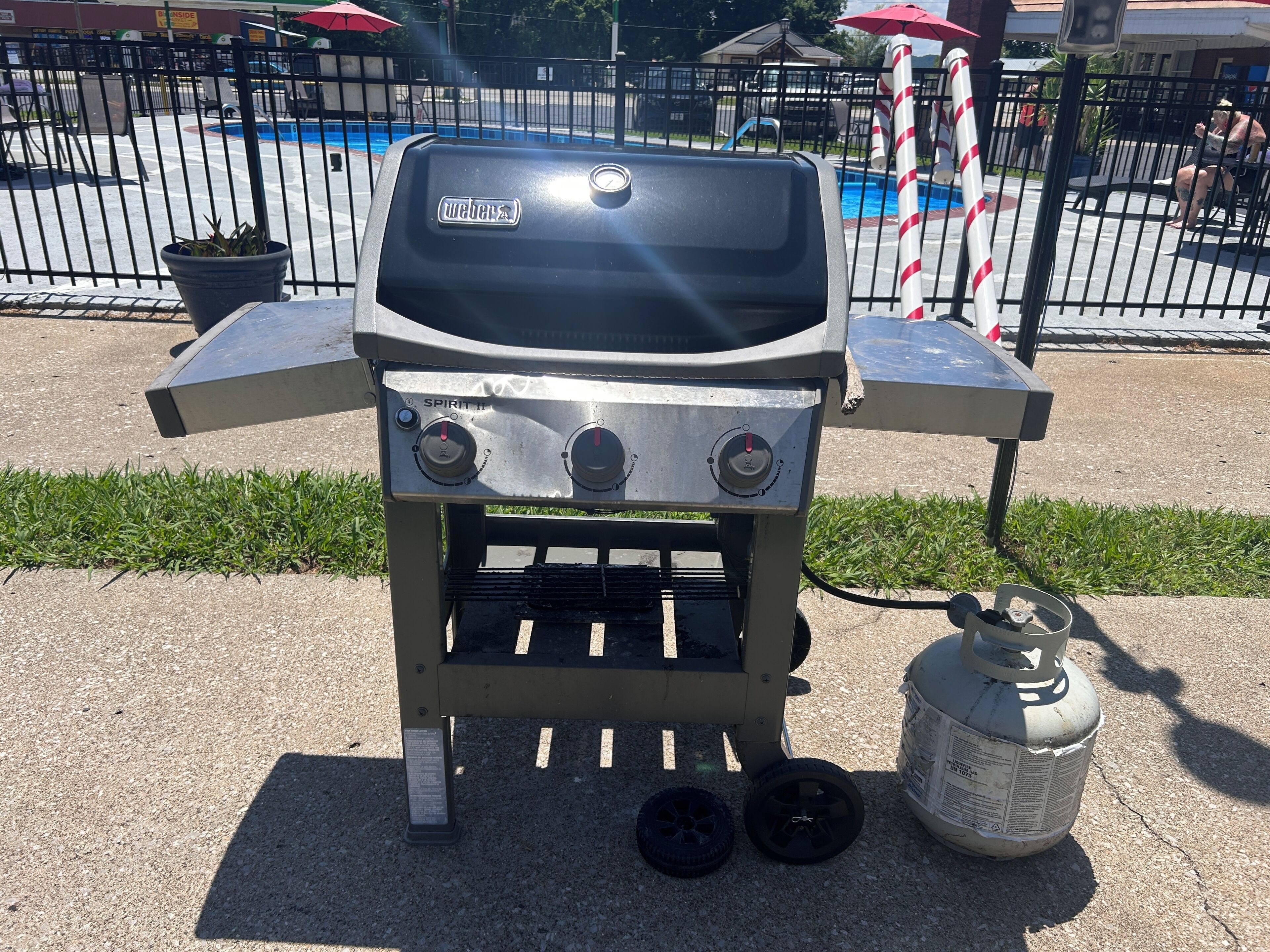 Ein Weber Spirit II Grill mit zwei Rädern, einer Propangasflasche und einer Poolumgebung.