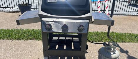 Ein Weber Spirit II Grill mit zwei Rädern, einer Propangasflasche und einer Poolumgebung.