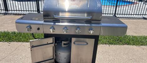 A portable stainless steel grill with four burners, a side shelf, and a storage compartment.