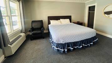 A bedroom with a bed, a chair, a nightstand, a mirror, and a window with curtains.