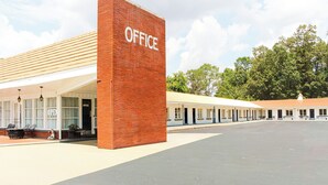 Un edificio con un llamativo letrero que dice 'OFFICE', un área de estar cubierta al aire libre y un estacionamiento.