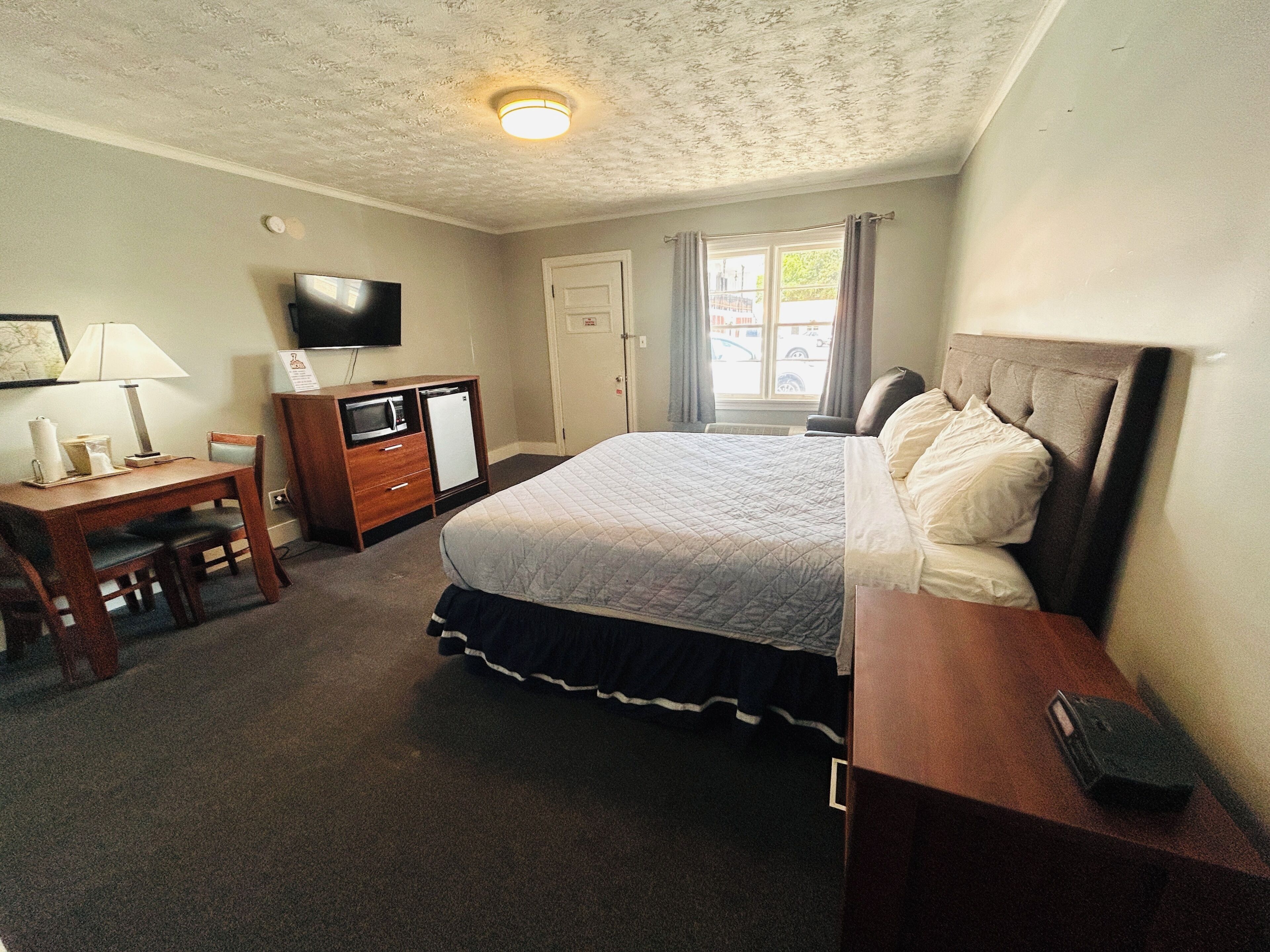 Un dormitorio con cama, escritorio, televisor, cómoda y ventana.
