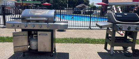 A poolside area with a barbecue grill and a gas station in the background.