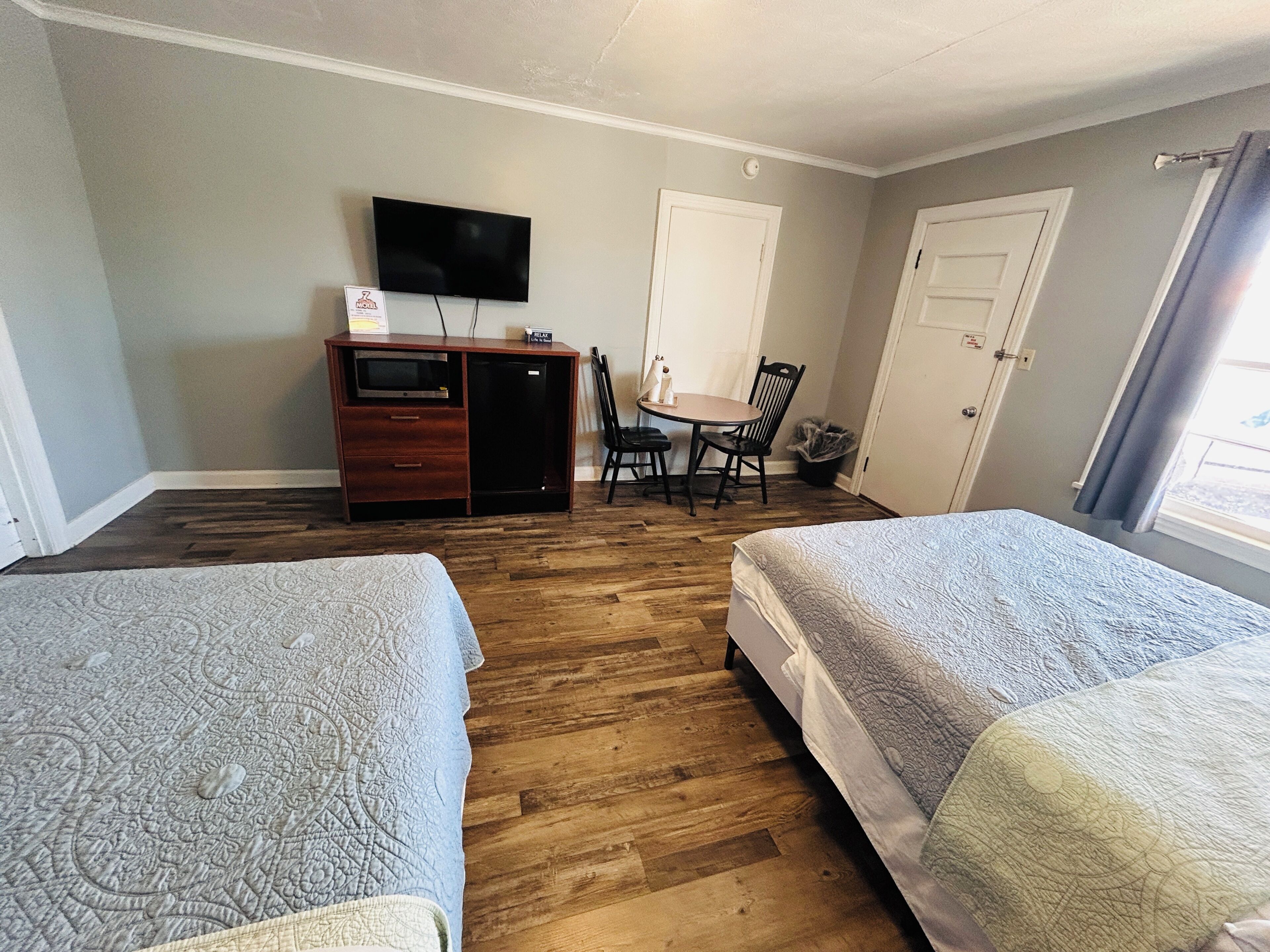 Une chambre d’hôtel avec deux lits, un bureau avec une télévision, une chaise et une petite kitchenette.