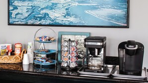 Una encimera de cocina con una cafetera, una máquina Keurig, una jarra de café y un cuadro enmarcado de un paisaje costero.