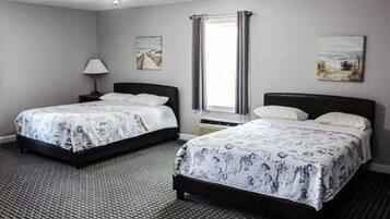 A hotel room with two beds, a ceiling fan, a window with curtains, and artwork on the walls.