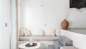 A modern living room with a sofa, a small table, and a TV mounted on the wall. - Aura 1-bedroom apartment with AC and WiFi in charming Thira (Thira)