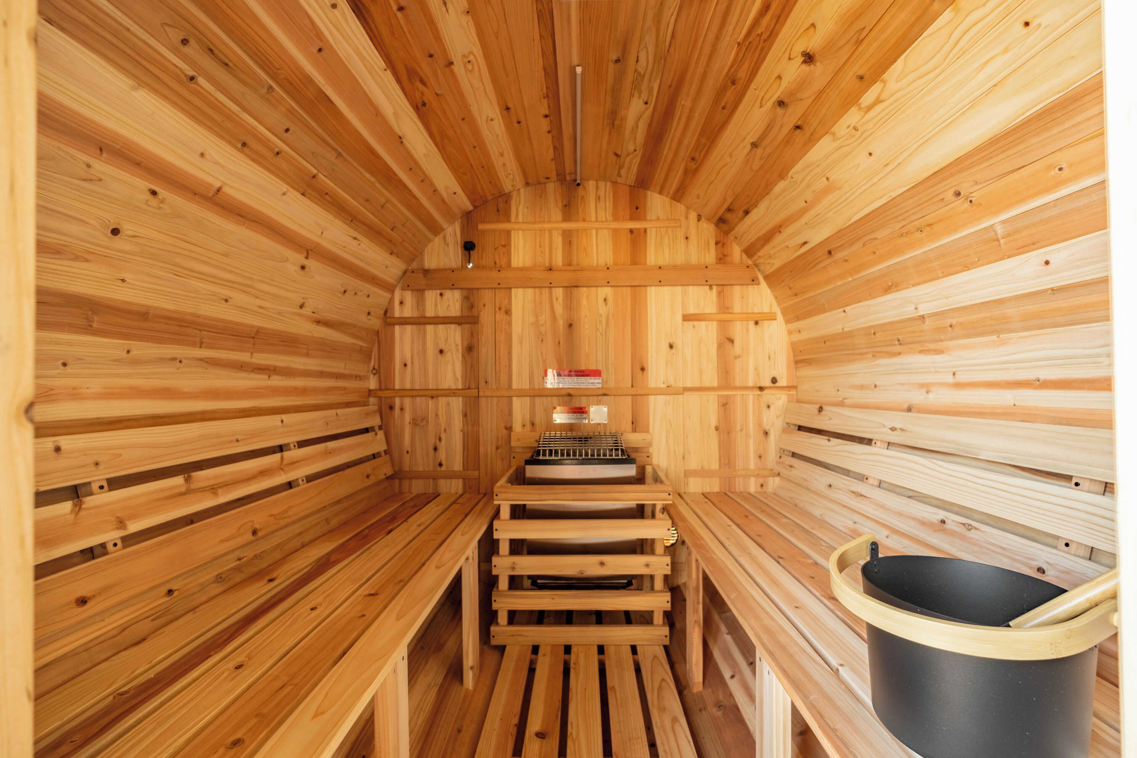 Una sauna con paredes y bancos de madera, un calentador central y un recipiente negro.