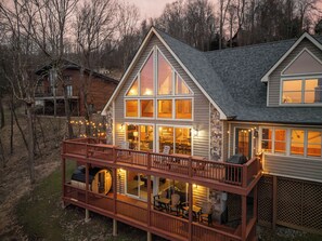 A two-story house with a balcony, large windows, and a deck with outdoor furniture. - Lake View Lodge with Hot Tub, Sauna, Fire Pit, Games, Gym, & EV Friendly (Oakland)