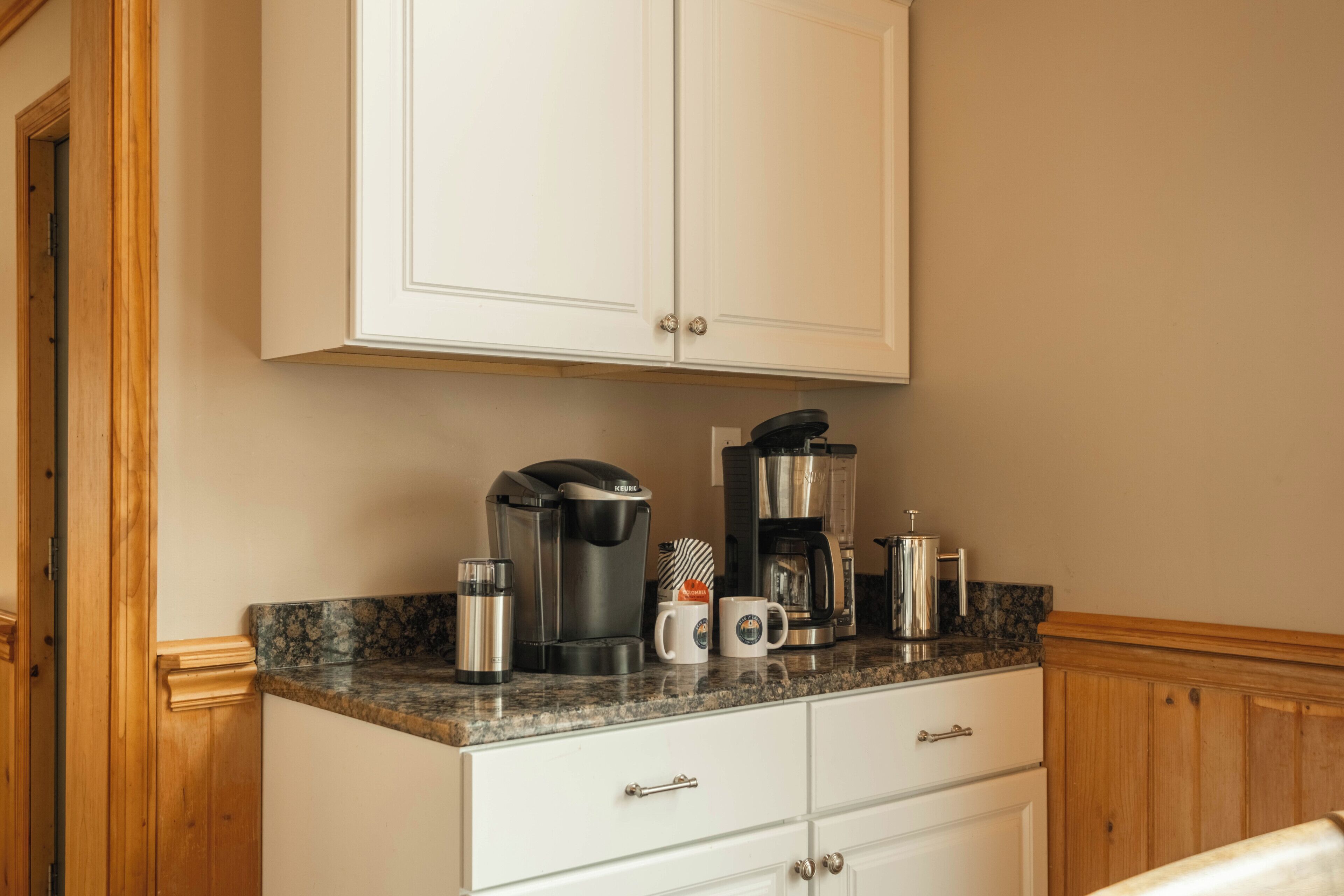 A kitchen with white cabinets, a granite countertop, and coffee-making equipment.