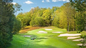 A golf course with a well-maintained green, sand bunkers, and a clear sky.