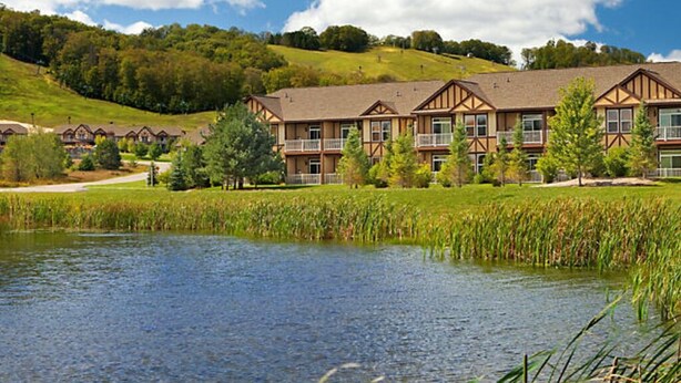 A hotel with a large building, a pond, and a hilly landscape.