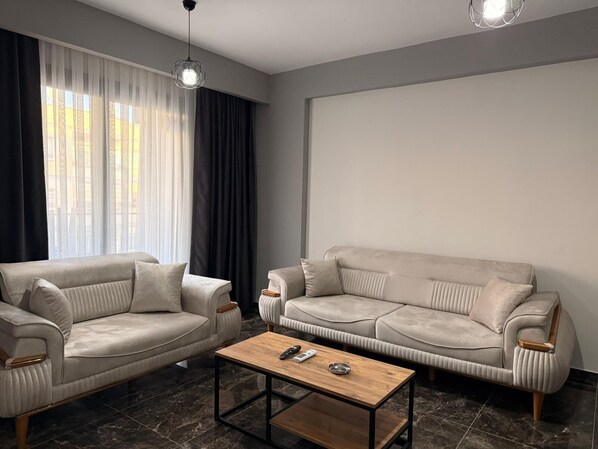 A modern living room with two sofas, a coffee table, and a large window with curtains.