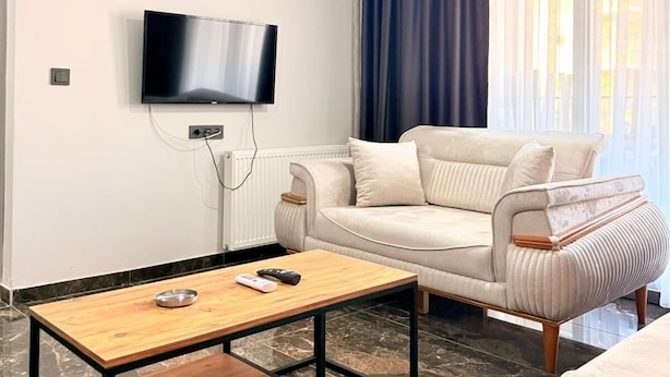 A modern living room with a sofa, a wooden coffee table, a flat-screen TV mounted on the wall, and an air conditioning unit. - BLACK HOUSE OTEL TURİZM  (Mersin)