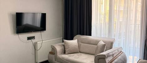 Una sala de estar moderna con un sofá, una mesa de centro, un televisor y una ventana con cortinas.