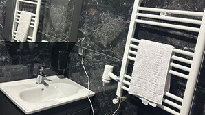 A bathroom with a white sink, a mirror, a towel rack, and black marble walls. - BLACK HOUSE OTEL TURİZM  (Mersin)