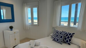 A bedroom with a bed, two windows, a white dresser, and a view of the beach. - PRECIOSO APARTAMENTO FRONTAL AL MAR - only families (Playa de Gandía)