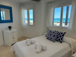 A bedroom with a bed, two windows, a white dresser, and a view of the beach. - PRECIOSO APARTAMENTO FRONTAL AL MAR - only families (Playa de Gandía)