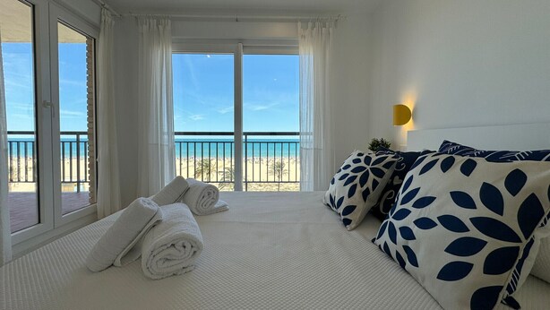 A hotel room with a bed, white towels, a view of the beach, and a balcony. - PRECIOSO APARTAMENTO FRONTAL AL MAR - only families (Playa de Gandía)