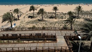 A beach with palm trees, a wooden boardwalk, and a view of the ocean. - PRECIOSO APARTAMENTO FRONTAL AL MAR - only families (Playa de Gandía)