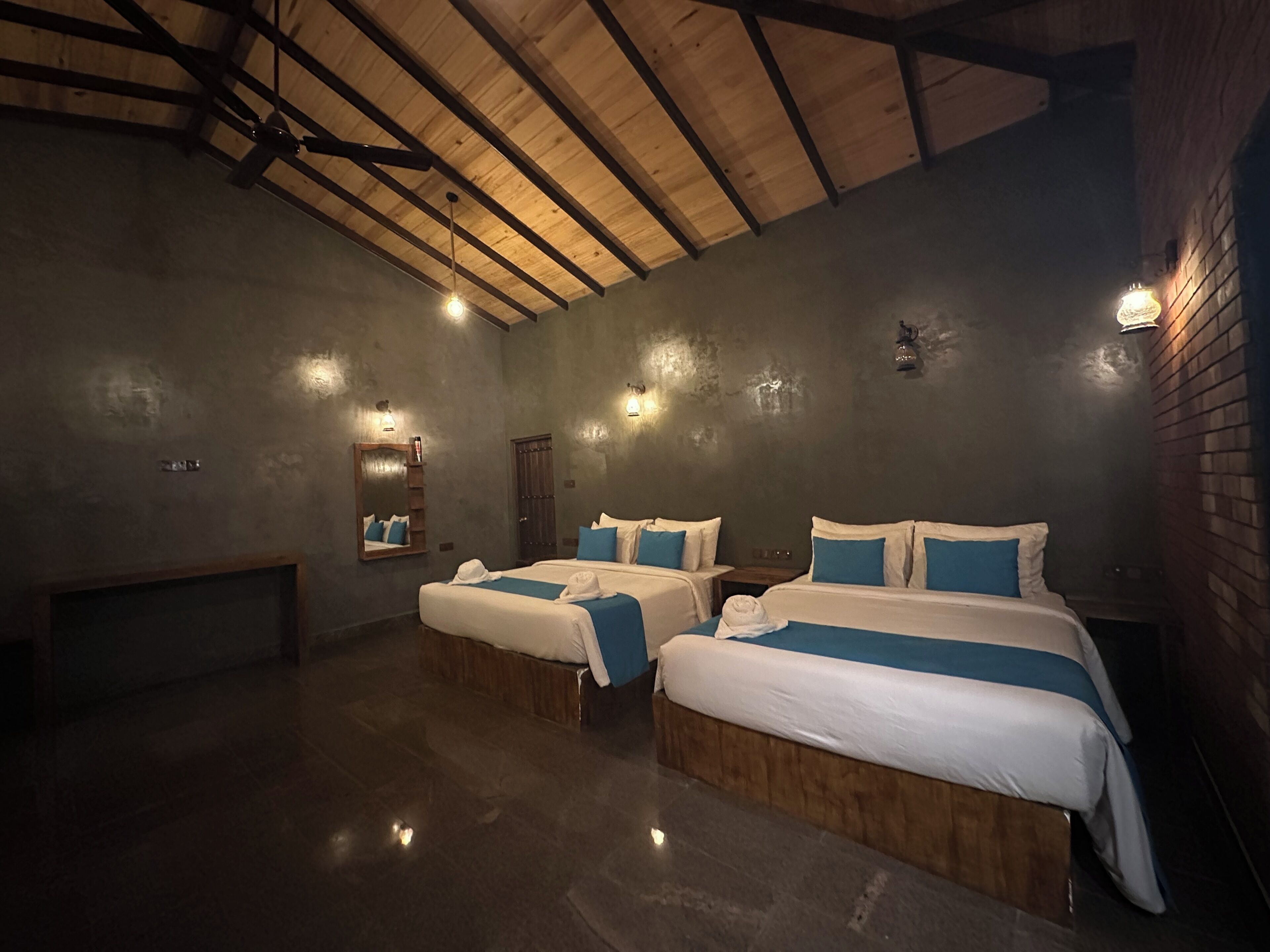 A hotel room with two beds, a wooden ceiling, and wall-mounted lighting.